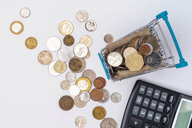 Монеты в тележке супермаркета и калькулятор на белом фоне концепция накопления богатства прибыли