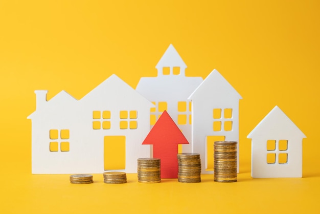 Coins on a table a red up arrow and house The concept of the rising price of real estate