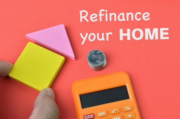 Photo coins toy house calculator over red background written with refinance your home