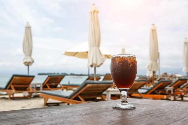 Photo cola glass on beach with umbrellas cooling drink