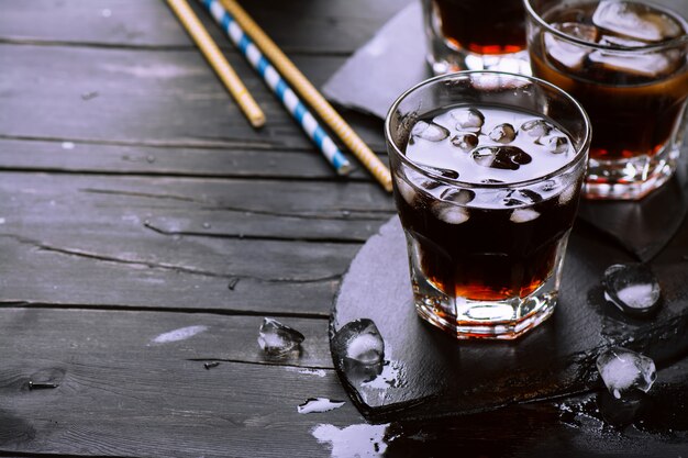 Cola with ice cubes in glasses on dark wooden table