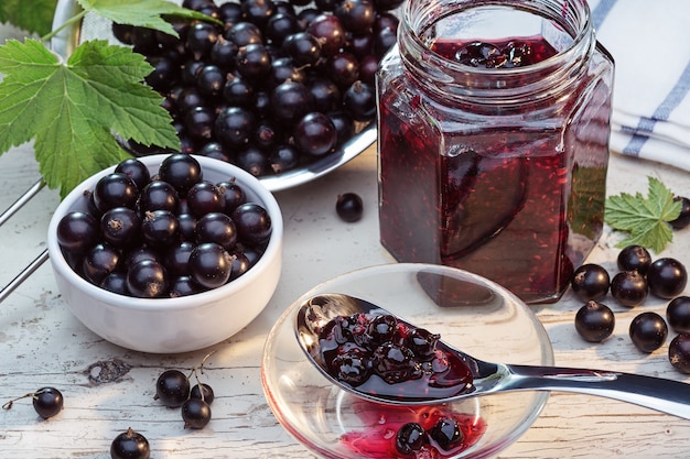 Colander and white bowl with fresh black currant and original leaves on wooden background Healthy food vitamins