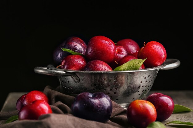 Colander with ripe juicy plums on dark background