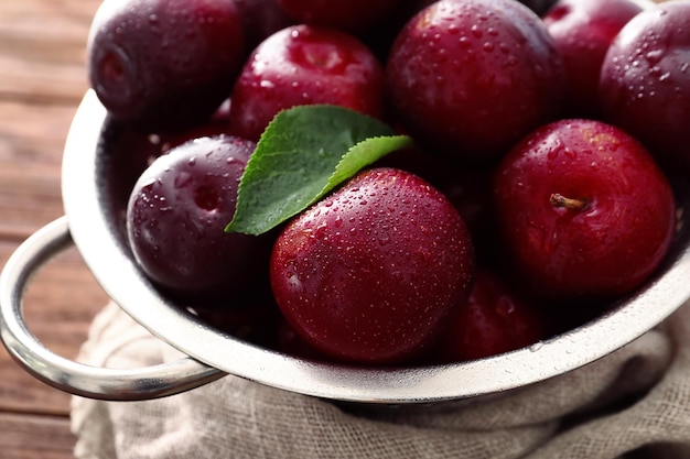 Colander with ripe juicy plums on table closeup