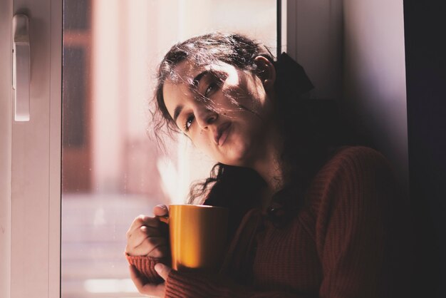 Cold autumn days  a young multiracial female drinks coffee in a cozy windowsill middleeastern or mix...