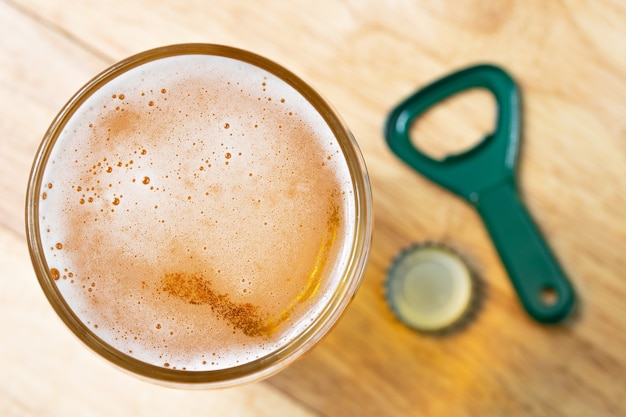 Photo cold beer bubble and opener top view on wood table