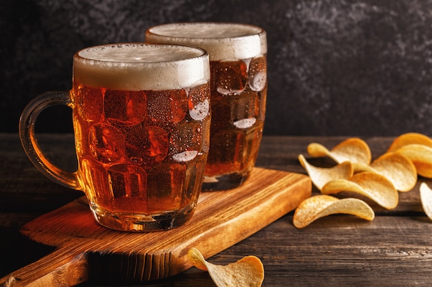 Cold beers in glass with chips on a dark surface