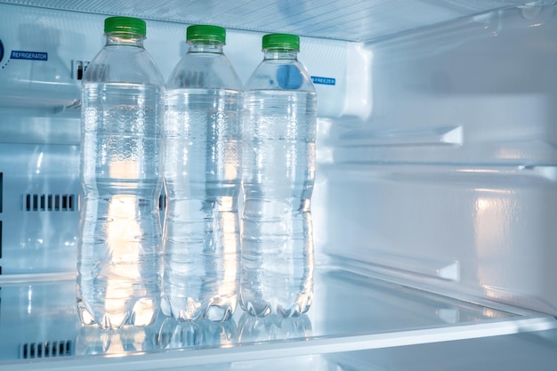 Cold bottles of clean drinking water in a white refrigerator