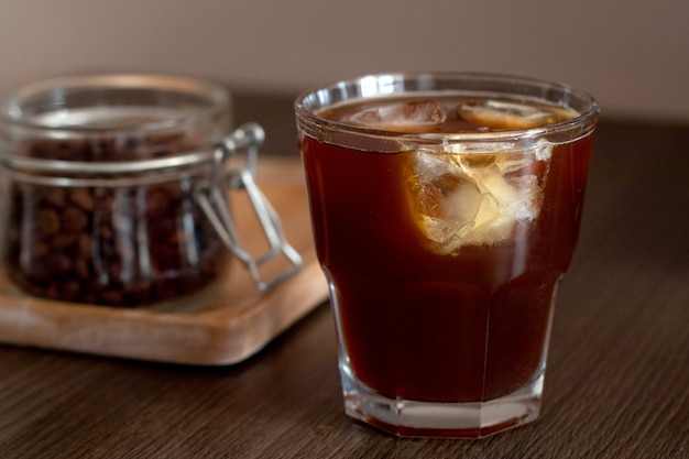 Cold brew Ice coffee with ice cubes and jar with coffee beans on wooden plate.