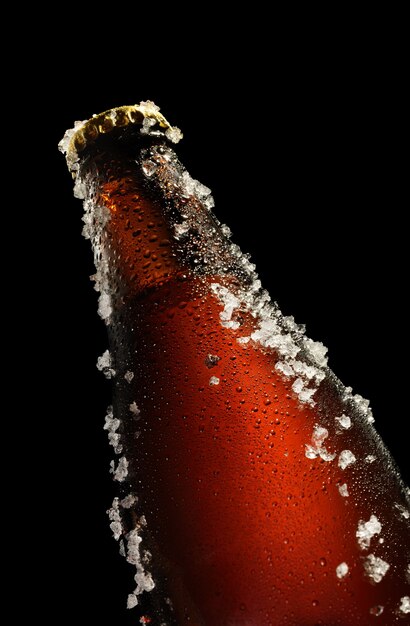 Cold brown bottle of beer with water droplets and ice