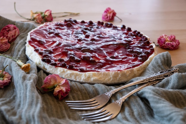 Foto cheesecake freddo con gelatina di ciliegie e rose intorno a esso servito su sfondo di legno con lancio verde e forchette antiche