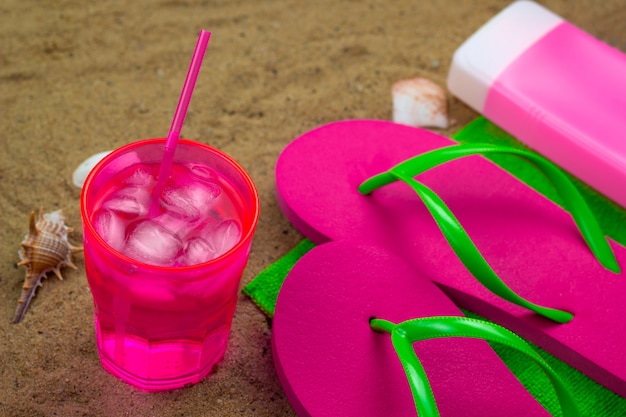 Cold coctail,slippers and sunblock on a green towel on a beach