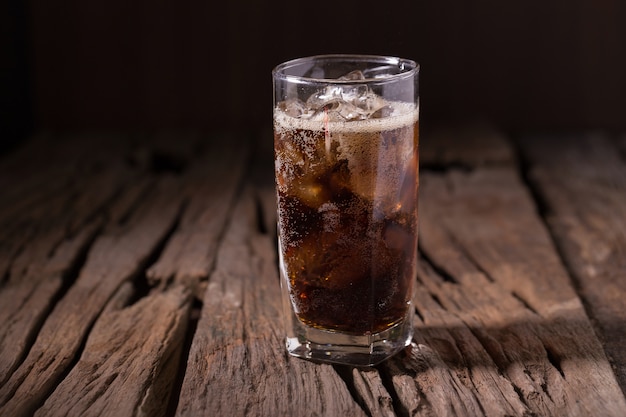 Cold Cola with ice in a glass on wooden background
