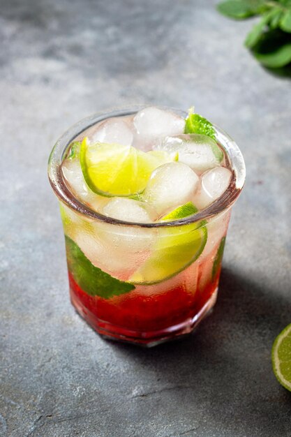 Acqua disintossicante fredda con menta fragola lime nel bicchiere con cubetti di ghiaccio su sfondo grigio da vicino