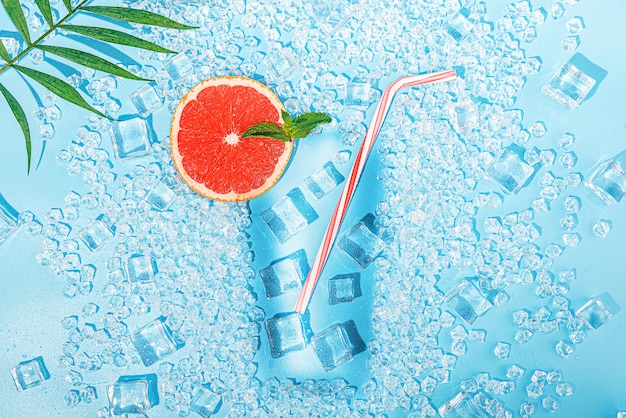 Photo cold drink. ice on a light blue background laid out in the form of a glass with a tubule for a cocktail and a slice of grapefruit