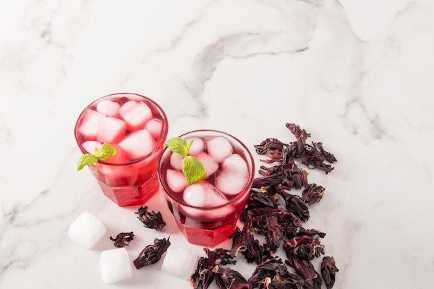 A cold drink made from hibiscus rose petals with ice cubes and\
mint on a marble table and dry rosebuds