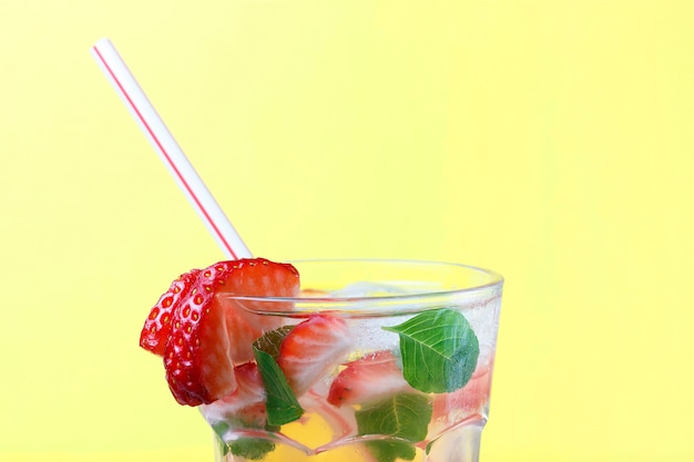 Cold drink with ice and strawberries, yellow summer background, front view, copy space