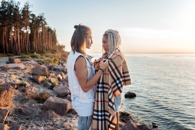 Cold evening. Caring loving man giving his girlfriend plaid on cold summer evening having rest near river