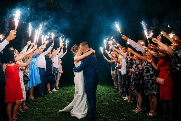 Cold fire from cake candles and fireworks in the hands of people around the newlyweds