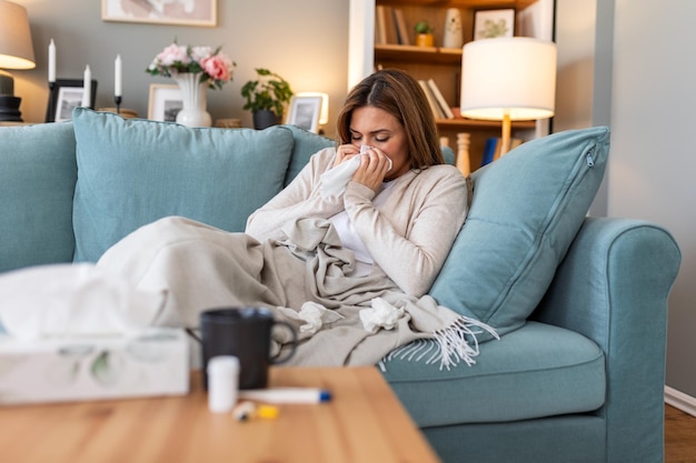 Photo cold and flu portrait of ill woman caught cold feeling sick and sneezing in paper wipe closeup of beautiful unhealthy girl covered in blanket wiping nose healthcare concept