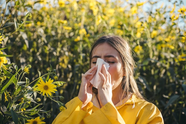 Cold flu season runny nose Flowering trees in background Young girl sneezing and holding paper tissue in one hand and flower bouquet in other Flu Allergy season