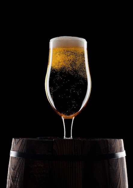 Cold glass of craft beer on old wooden barrel on black background with dew and bubbles