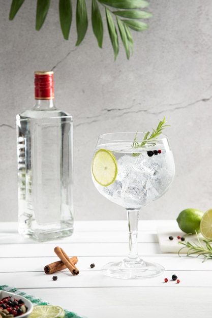 Фото Холодный стакан джин-тоника и бутылка на белой деревянной основе на светлом фоне вертикальный формат