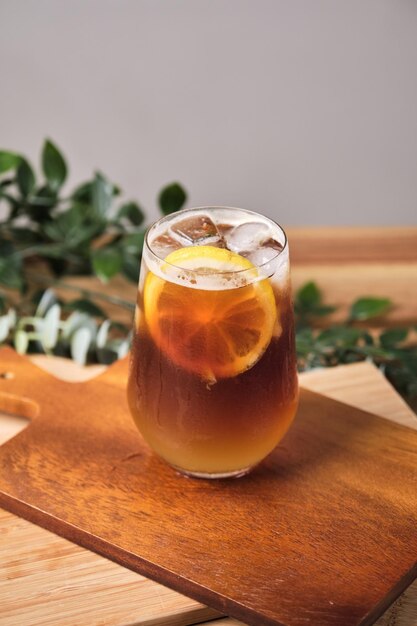 Cold iced black brew coffee mixed lemon juice and lemon slices in a glass with pieces of ice on a wooden table natural light fresh summer drink in the morning