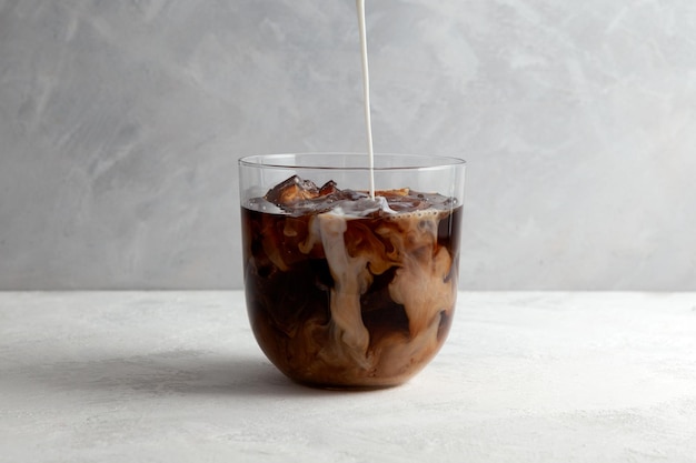 アーモンドミルク入りの冷たいアイスコーヒーさわやかな飲み物を透明なグラスに注ぎます