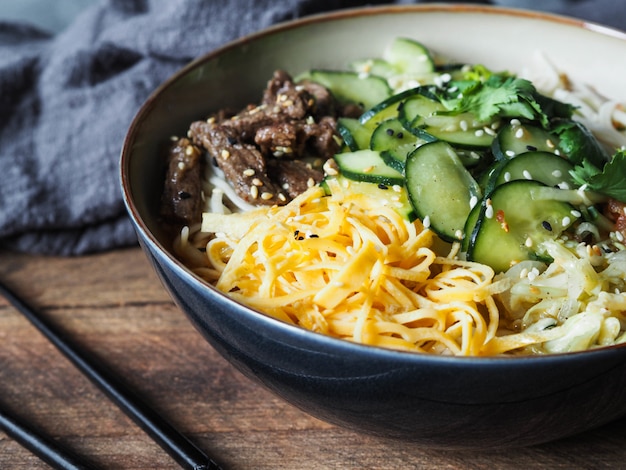 Cold Korean kuksi soup with vegetables, scrambled eggs, beef and noodles in a bowl and chopsticks