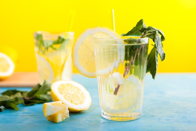 青いビンテージデスクの黄色の背景の上に暑い夏の日の冷たいレモン水ドリンク