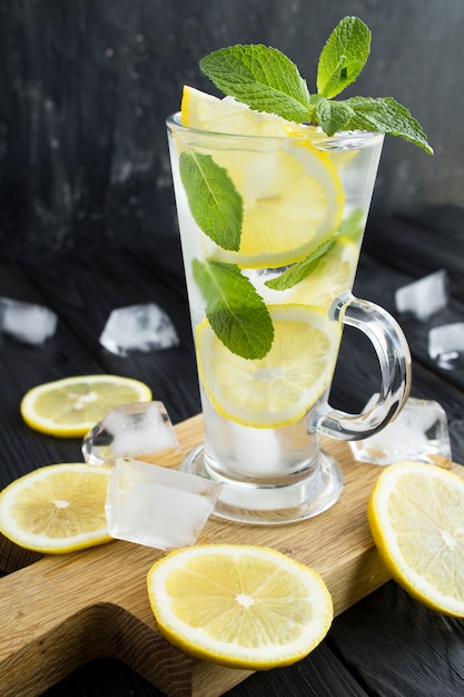 Холодный лимонад или настоянная вода с лимоном и мятой в стакане на темном фоне. Крупный план. Расположение вертикальное.