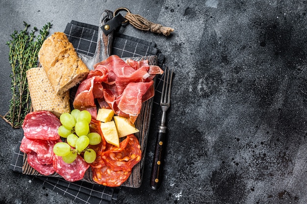 ハムプレート、豚肉-パンとブドウを添えた木の板に伝統的なスペインのタパス。黒いテーブル。上面図。