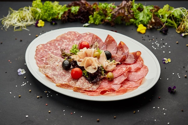 Cold meat platter ham sausage salami parma prosciutto bacon on cutting board with herb and olives over dark background Meat appetizer set of wine close up