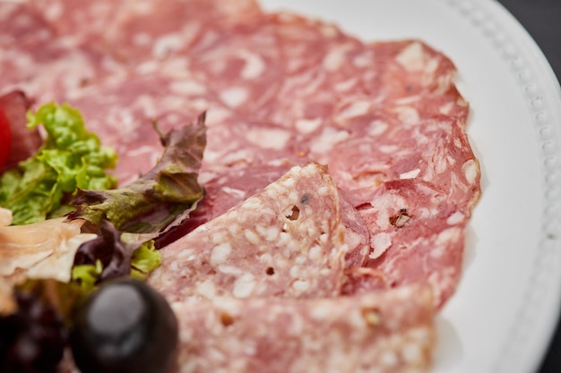冷たい肉の盛り合わせハムソーセージサラミパルマ生ハムベーコンまな板にハーブとオリーブと暗い背景の上にワインの肉前菜セットをクローズアップ
