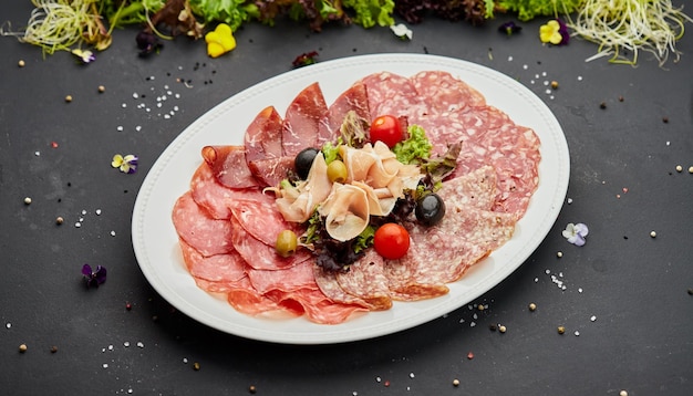 Cold meat platter ham sausage salami parma prosciutto bacon on\
cutting board with herb and olives over dark background meat\
appetizer set of wine close up