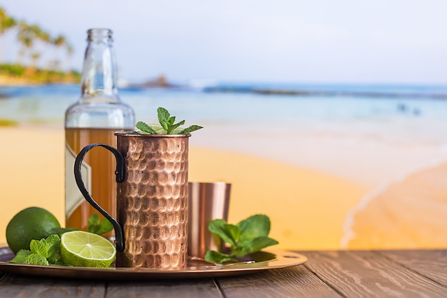 Cold Moscow Mules cocktail with ginger beer, vodka and lime over beach and seaside surface