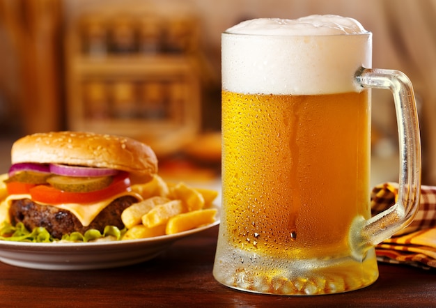 Cold mug of beer with hamburger on wooden table