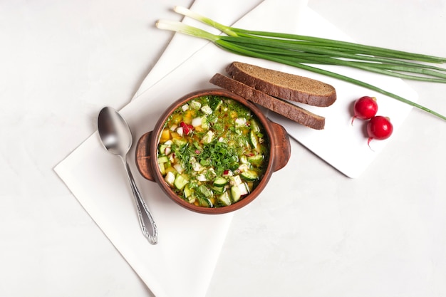 Cold okroshka with fresh vegetables and meat in a clay cup stands on a gray