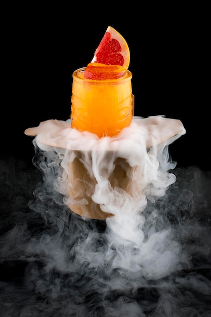 Cold orange lemonade surrounded by smoke on a dark background