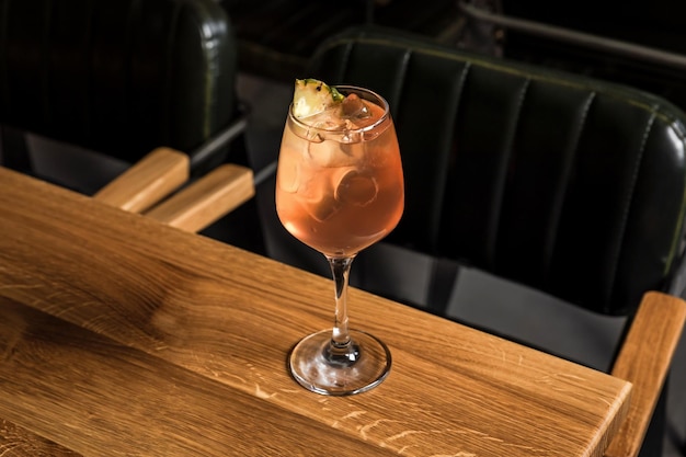 A cold refreshing low abv cocktail served in a wine glass with ice cubes garnished with dried pineapple slice on a wooden table at the bar or restaurant