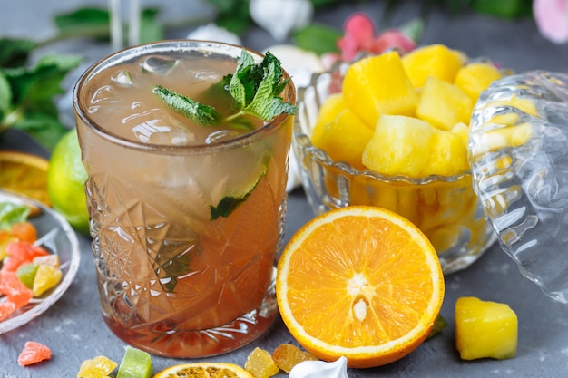 Cold refreshing pineapple cocktail with lime and mint for a hot summer day on a gray background decorated with candied fruit, mint and pineapple cubes.