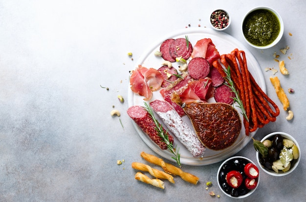 Cold smoked meat plate. Traditional italian antipasto, cutting board with salami, prosciutto, ham, pork chops, olives on grey. Top view, copy space, flat lay