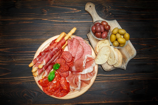 Cold smoked meat plate with pork chops, prosciutto, salami and bread sticks