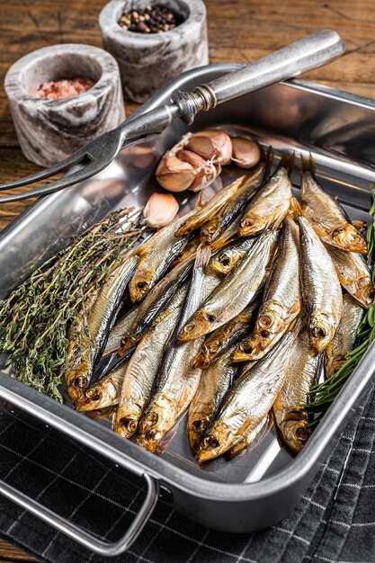 Cold Smoked sprat fishes in a kitchen tray with spices. Wooden background. Top view.