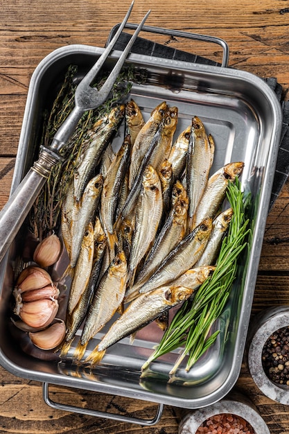 Cold Smoked sprat fishes in a kitchen tray with spices Wooden background Top view