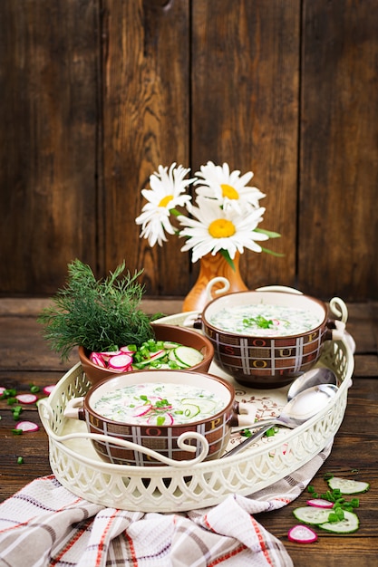 Cold soup with fresh cucumbers, radishes with yoghurt in bowl on wooden table. Traditional russian food - okroshka. Vegetarian meal.