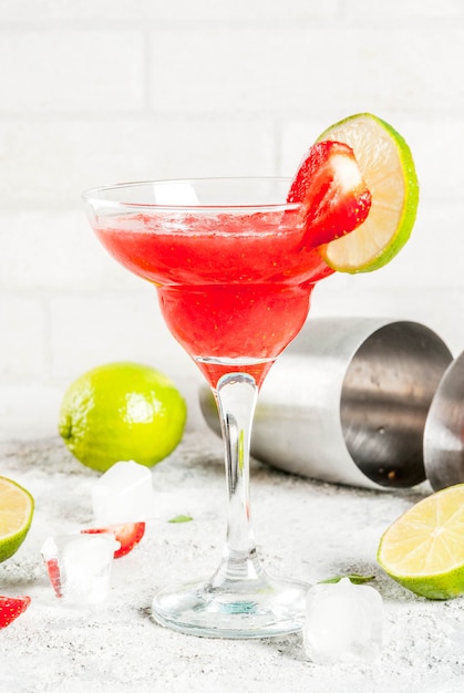 Cold strawberry margarita cocktail with ice, lime and fresh berries in margarita glass