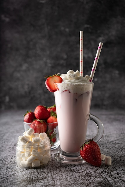 A cold strawberry milkshake with fresh strawberries and cream in a high transparent glass