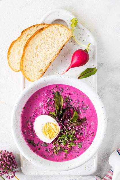 Cold summer soup of beets, cucumbers and eggs in a white plate on a white stone table. Top view. Copy space.